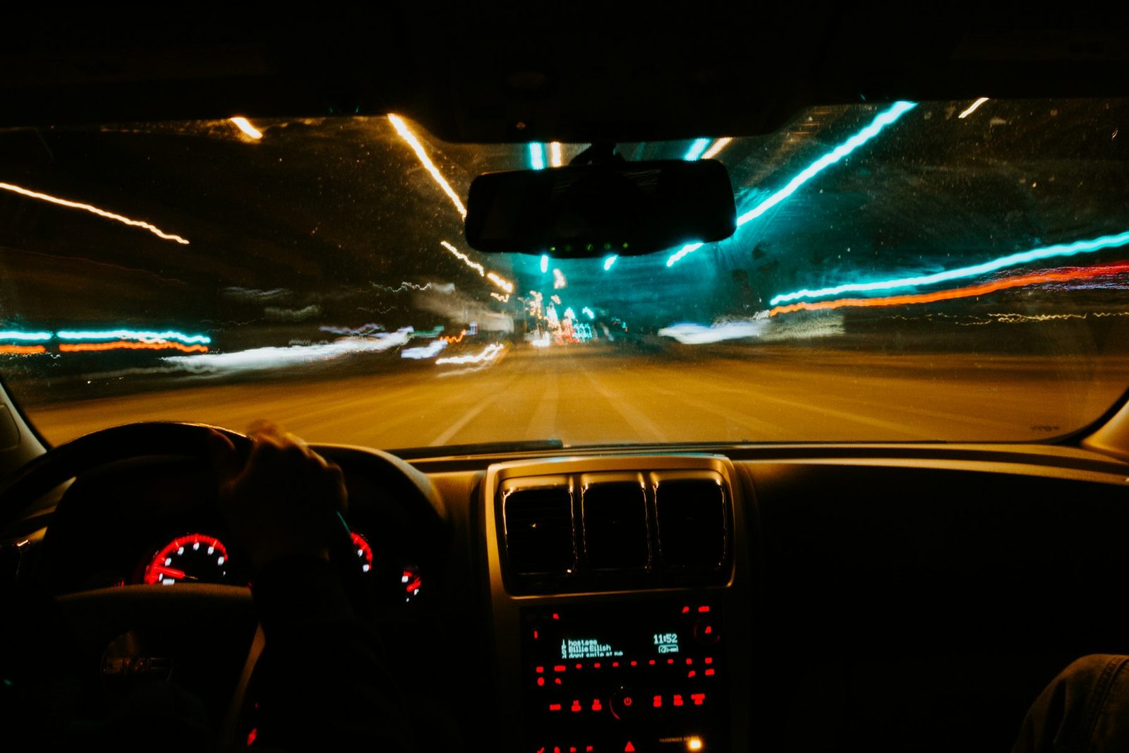 Blick aus dem Fahrzeuginneren durch die Windschutzscheibe bei Nacht, Lichtspuren einer beleuchteten Straße